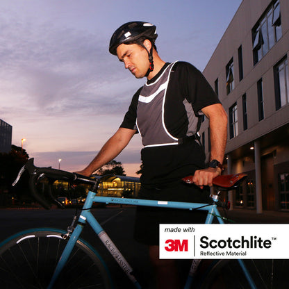 Person standing next to bike in low lighting wearing bike helmet and sports vest. 