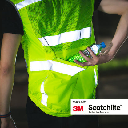 Person standing outside wearing yellow vest and putting water bottle in back pocket of vest